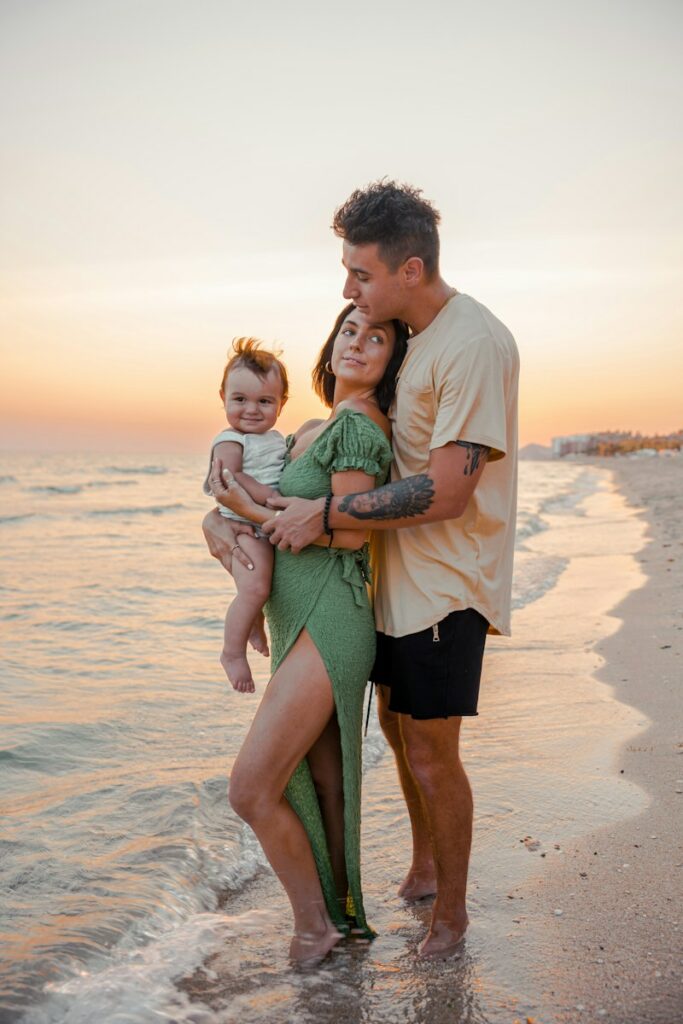 a man and woman holding a baby on the beach